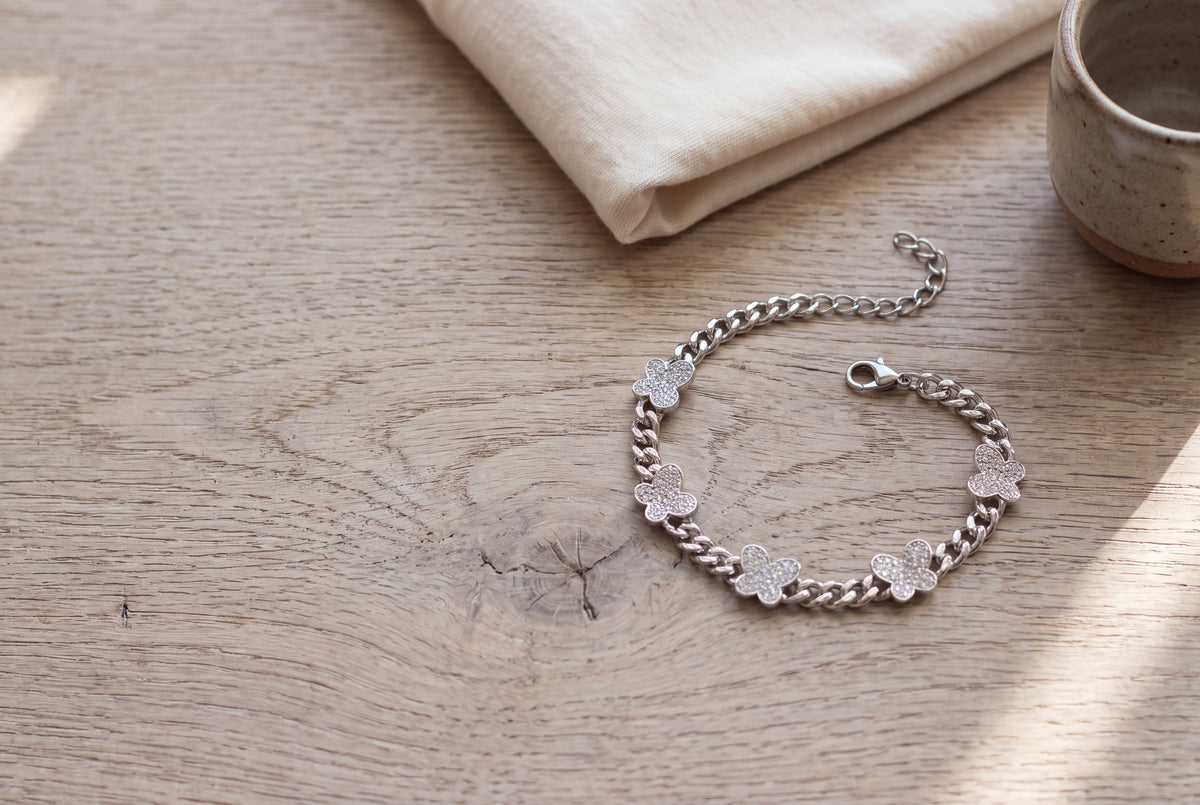 Sterling silver curb bracelet with pavé moissanite butterflies on a pale oak table