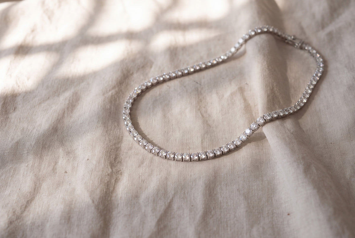 Moissanite tennis necklace in sterling silver laid on washed oat linen in morning light